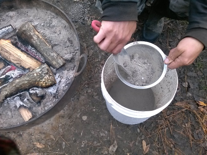 sifting wood ashes into plastic bucket